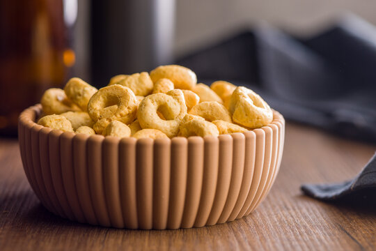 Bowl of Crunchy Taralli Snack Rings on Wooden Table With Bottles in Soft Background