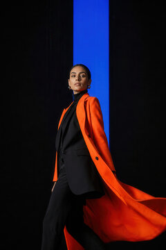 Fashionable woman wearing an orange coat against a blue background