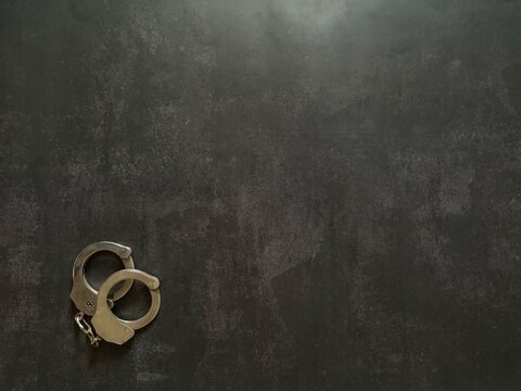 Metal handcuffs on a dark textured background representing law enforcement, justice and public safety concepts.