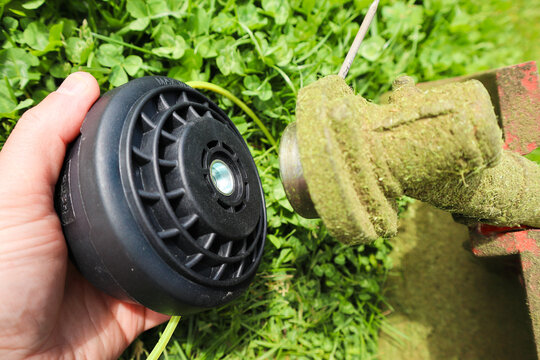 Hand holding string trimmer head replacement next to gearbox shaft