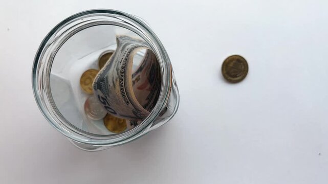 Saving money in a glass jar, accumulating coins and fifty dollar bills for future investments, wealth management, and financial planning, isolated on a white background
