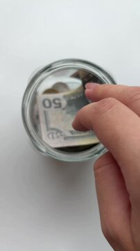 Person putting fifty us dollar bill into a savings jar for financial security and wealth accumulation, isolated on a white background, symbolizing economic planning
