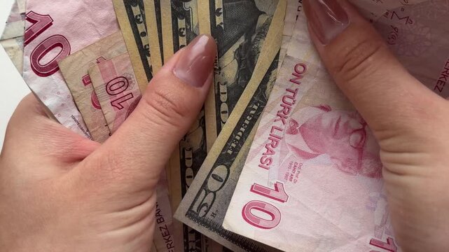 Woman's hands counting turkish lira and us dollar banknotes, symbolizing currency exchange, international trade, inflation, and global finance on a white background