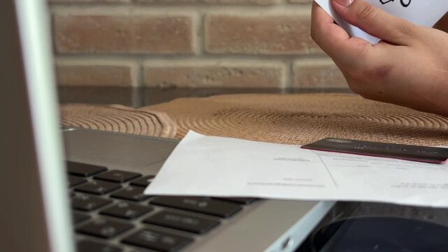 Woman's hands placing cash money into an envelope marked savings for financial planning, budgeting, and future investment while sitting at a desk with a laptop
