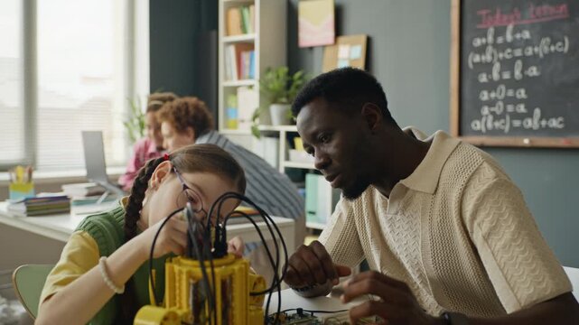 African American male teacher guiding Caucasian kid assembling robotics kit in modern classroom. Footage is ideal for STEM education marketing and school promotional videos