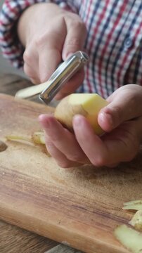 Vertical video. Female hands peeling raw potato. 