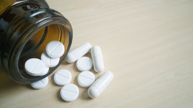Assorted pills spilled from bottle on light background.