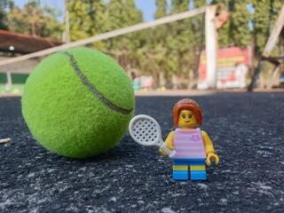 Obraz premium Indonesia - August 31, 2024 : Mini toy of action figure at tenniscourt with blurred background. Sport photography concept design. Miniature Young girl with tennis ball and racket.