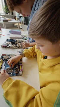 Vertical video of Caucasian kid assembling computer motherboard during STEM class with African American classmate. Footage is ideal for marketing modern school education and technology programs