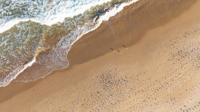 Aerial view of Dee Why Beach with gentle waves washing onto the sandy shore and people walking along the coastline in Dee Why, New South Wales, Australia.
