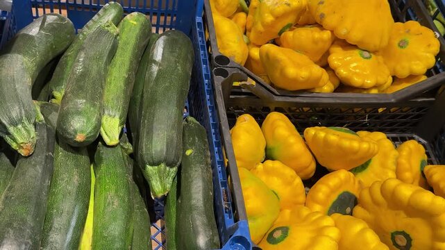 Fresh yellow pattypan squash and dark green zucchini arranged in neighboring wooden crates create a colorful vegetable display for markets, grocery stores and everyday shopping. Close up.