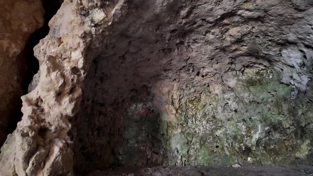 Xemxija, Malta 29.07.2026 - Heritage trail, Roman Baths, shelf like cut in the stone Dark cave walls show rough, textured surfaces. Greenish moss grows on damp, uneven stone. Light filters through nar