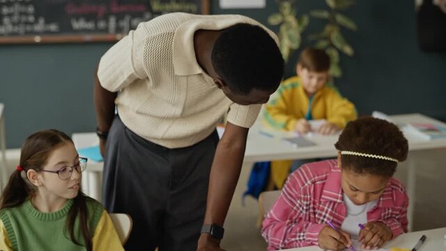 African American male teacher helping multiethnic kids with schoolwork in modern classroom. Clip can be used in promotional videos for schools, tutoring services, or educational programs