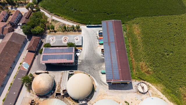 Aerial view of an Italian cattle farm with solar panels on barn roofs and a biomethane production facility with storage domes, surrounded by agricultural fields in Lodi, Lombardy, Italy.
