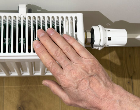 Hand adjusting a radiator thermostatic valve in a home interior. Heating control for temperature regulation and energy saving. Indoor maintenance concept for winter comfort..