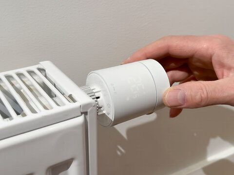 Hand adjusts a thermostatic radiator valve on a white heater. Close up of home heating control in a clean interior. Energy saving temperature regulation for winter comfort..