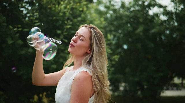 Woman blows bubbles in sunny park. She smiles brightly, enjoying peaceful moment. Bubbles float gently around her. Perfect for joyful, summer, or childhood-themed projects