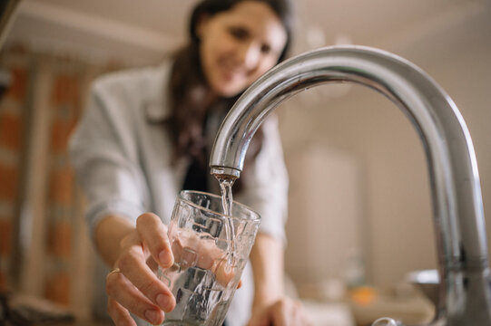 Woman filling water from faucet in glass at home