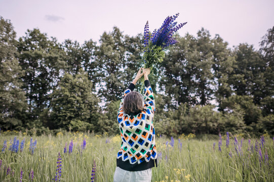 Joyful woman lifts a lupine bouquet outdoors in a summer field