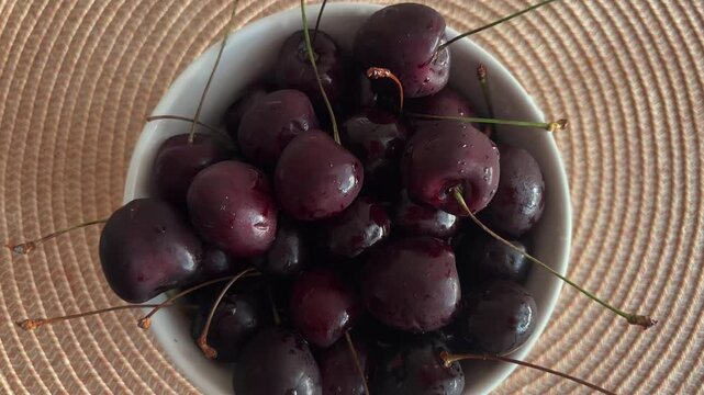 Fresh organic sweet cherries in a white bowl rotating on a table mat top view. Healthy delicious ripe red fruit for a vegan diet, covered with water drops for freshness