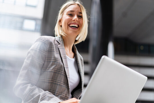 Portrait of happy young businesswoman with laptop in the city