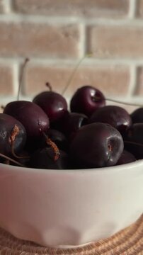 Fresh ripe cherries in a white bowl with a brick wall background showing organic summer fruit and healthy vitamins for a balanced diet and delicious dessert