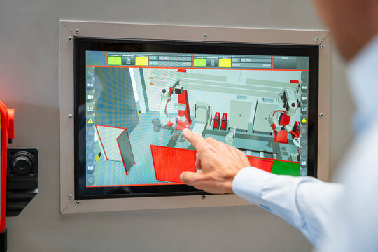 Man points at touchscreen showing industrial robot simulation