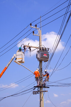 Electrician lineman workers with crane truck are repairing power lines and transformer on electric power pole against blue sky background in vertical frame