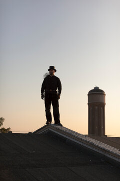Germany, chimney sweep standing on rooftop at twilight