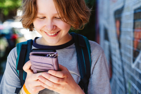 Smiling teenage girl uses a smartphone outdoors in the city