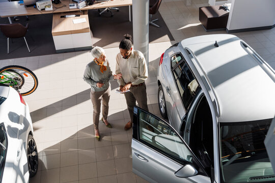 Salesperson discussing over document with customer near car at showroom