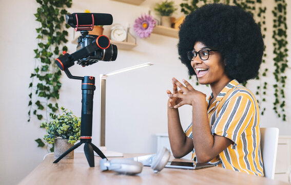 Cheerful female influencer with hands clasped vlogging at home