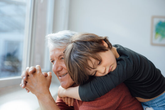 Thoughtful boy embracing grandfather at home