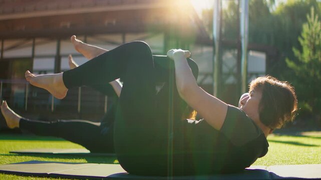 Elderly women practicing slow motion Pilates exercises outdoors on yoga mats, focusing on core strength, balance, and flexibility in a peaceful green environment