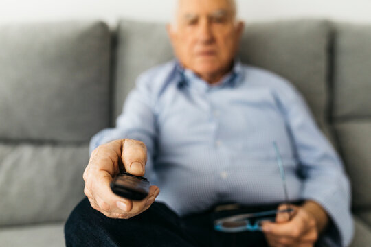 Senior man watching TV from the couch at home, focused on hand