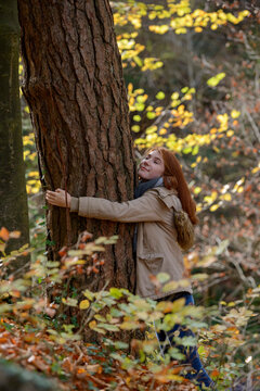 Smiling teenage girl hugging tree trunk in autumnal forest