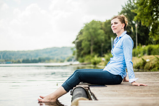 Woman sitting on jetty at a lake with feet in water