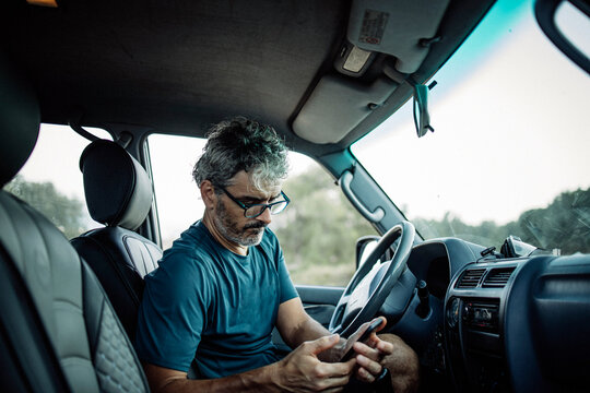 Mature man sitting sitting in his off-road vehicle checking his smartphone
