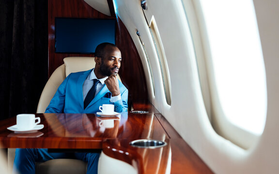 Young businessman with hand on chin looking through window while sitting in private jet