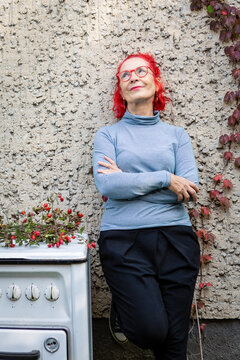 Portrait of smiling senior woman with red dyed hair leaning against house front