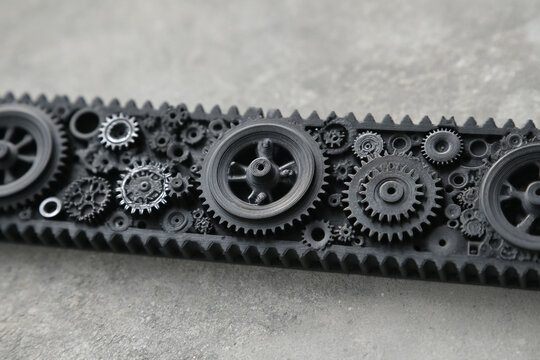 Detailed horizontal close up shot of complex black mechanical gears cogs wheels and toothed rack mechanism components system over grey concrete background, industrial heavy machinery engineering.