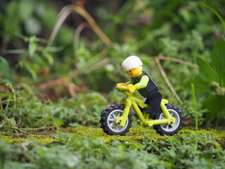 Obraz premium Indonesia - May 14, 2022 : Mini toy of action figure at grassland with blurred background. Miniature photography concept. Bicycle at outdoor with green grass conceptual design.
