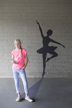 Portrait of smiling blond girl with smartphone and shadow of ballerina in the background