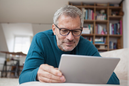 Mature man at home lying on couch using digital tablet