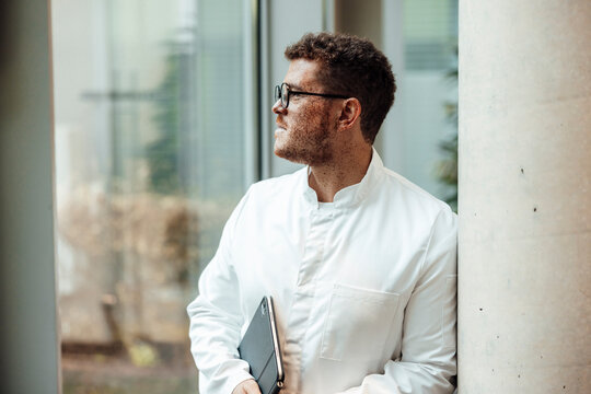 Doctor with freckles in lab coat holding tablet at hospital window