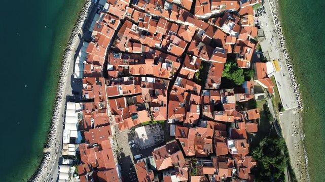 Top down drone view of the historic old town of Piran with red tiled rooftops, narrow streets, beach and Adriatic Sea coastline on a sunny summer day in Slovenia.