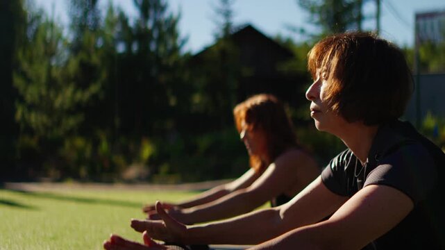 Slow motion outdoor Pilates session with two elderly women stretching on exercise mats, focusing on mindful movement, balance, and gentle senior fitness