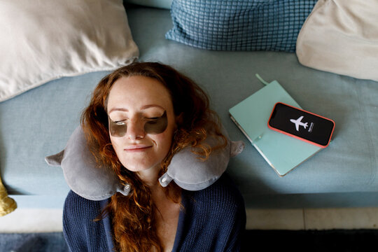 Redhead woman leaning head on sofa with smart phone on airplane mode in living room at home