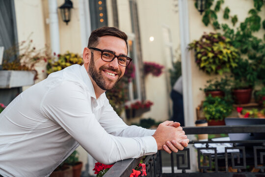 Smiling businessman with eyeglasses leaning on railing in office balcony