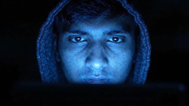 Man in Hoodie Staring at Computer Screen in Dark, Blue Light Glow
